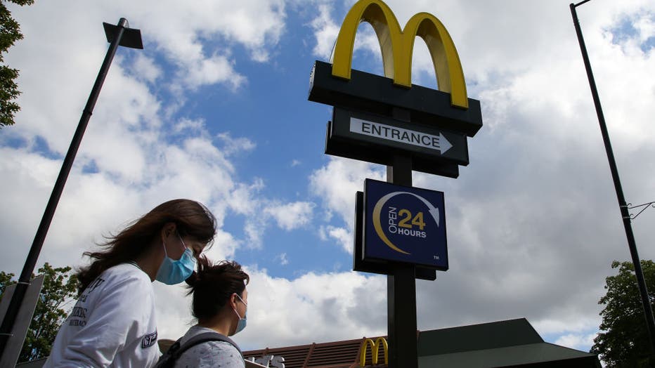 Women wearing face masks walks past a McDonald's logo