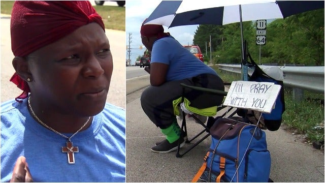 Woman sits along highway, holds 'I'll pray with you' sign
