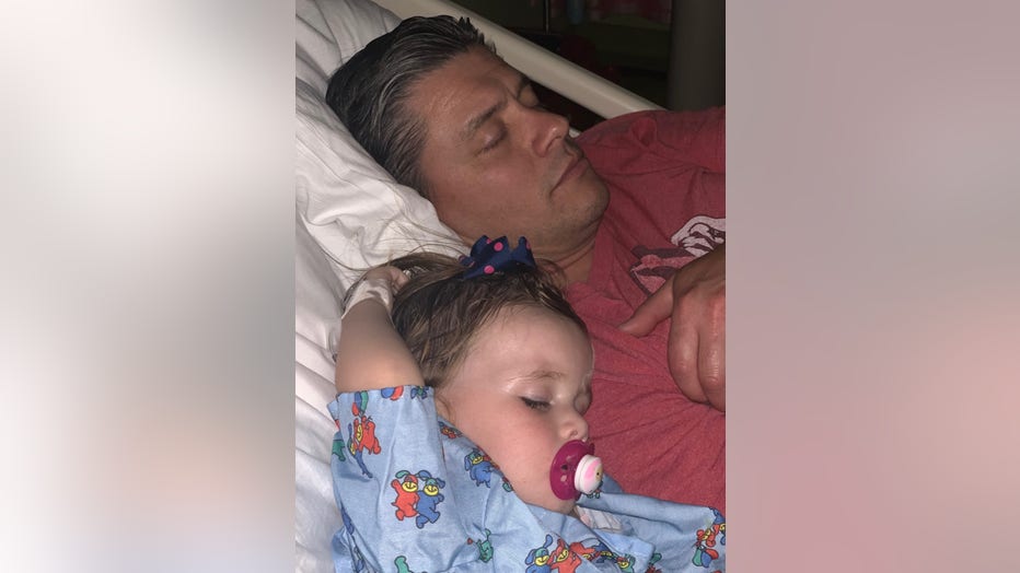 Toddler sleeps in a hospital bed next to her father.