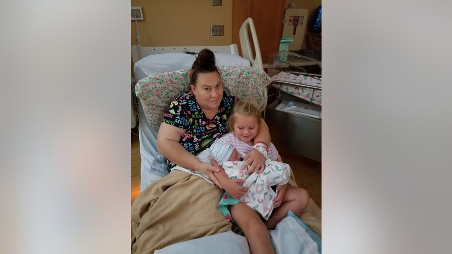 Mother holds daughter and baby in hospital bed.