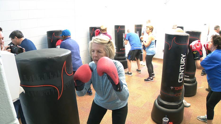 Woman in boxing gloves stands in front of punching bag.
