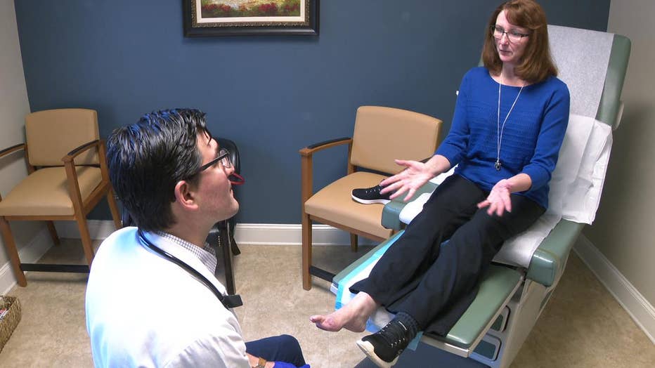 Doctors sits in exam room with woman, looking at her toe.