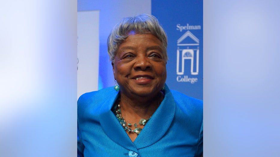 Woman smiles at the camera, standing in front of Spelman College sign