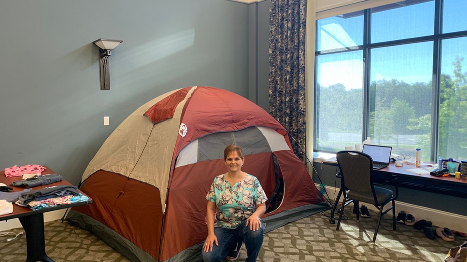 Woman kneels in front of tent where she has been sleeping inside senior community.