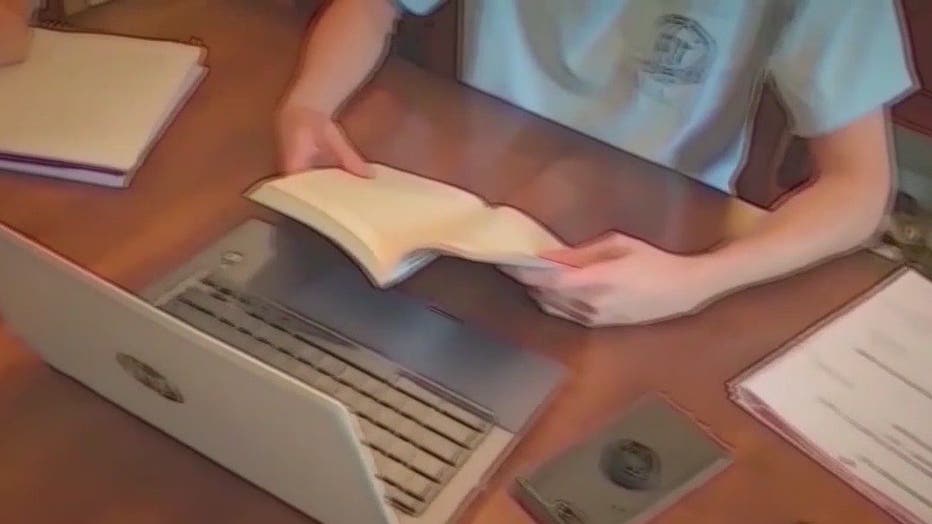 Student sits in front of a laptop, reading a book.