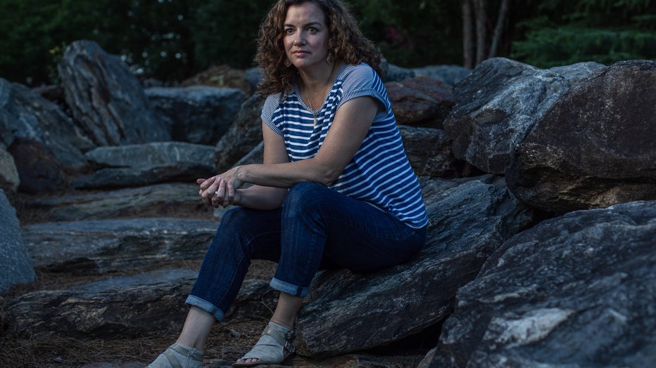 Woman sits against some rocks, with her arms resting on her knees.