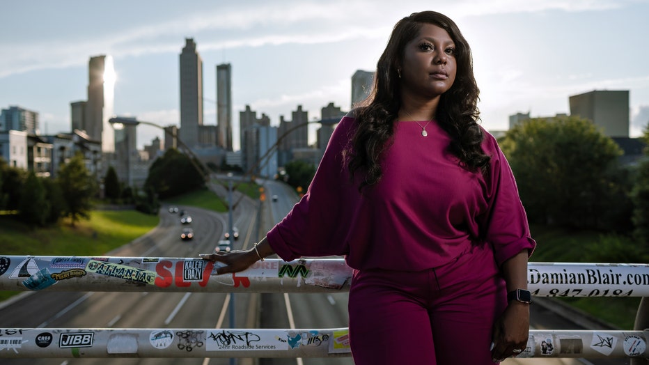 Woman stands on bridge, with the city of Atlanta in the background behind her. She looks confident and happy.