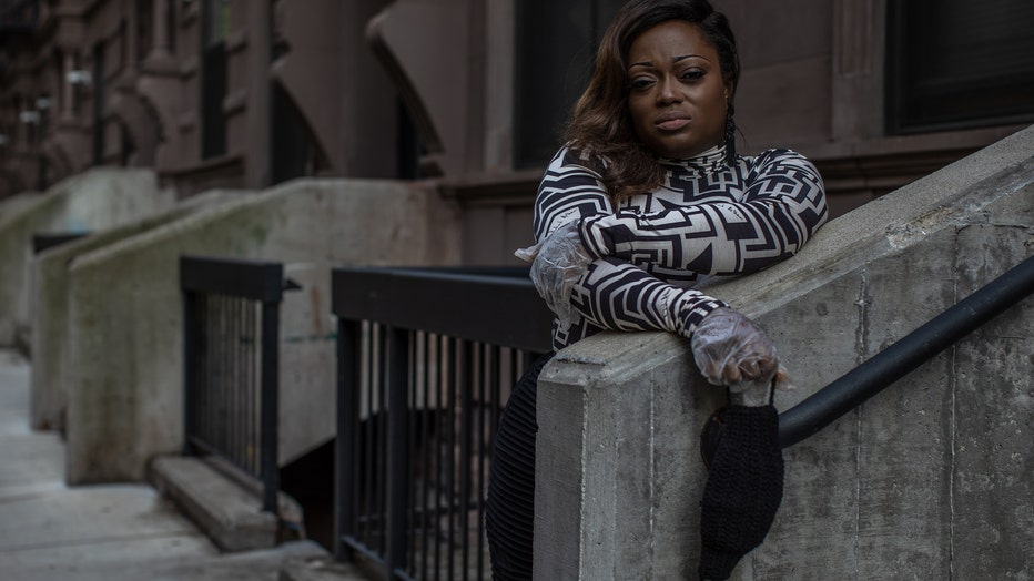 Woman in New York leans against a wall in front of a brownstone house. Her arms are crossed, and she looks relaxed.