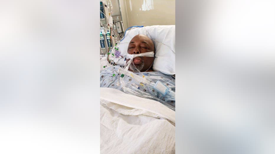 Man lies in ICU bed on a ventilator, with his eyes close.