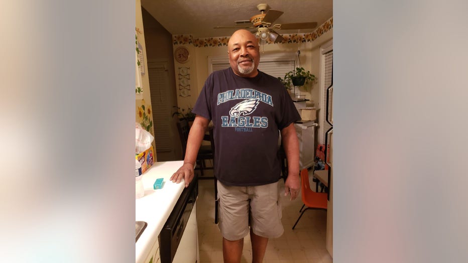 Man leans against kitchen counter. He is smiling and wearing a Philadelphia Eagles t-shirt