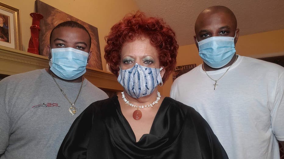 Woman wearing mask stands between her two adult sons, who are both wearing masks.