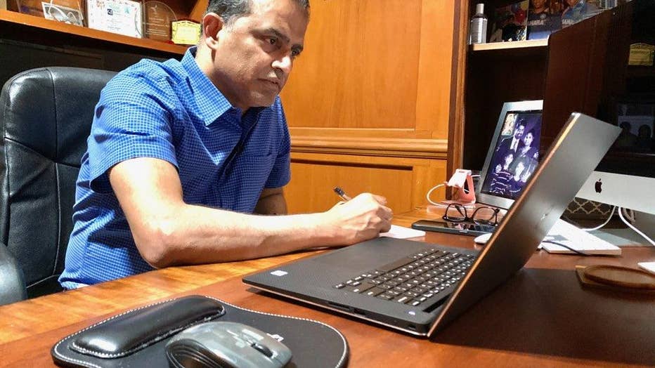 Indian American doctor sits in a wood-paneled home office on laptop.