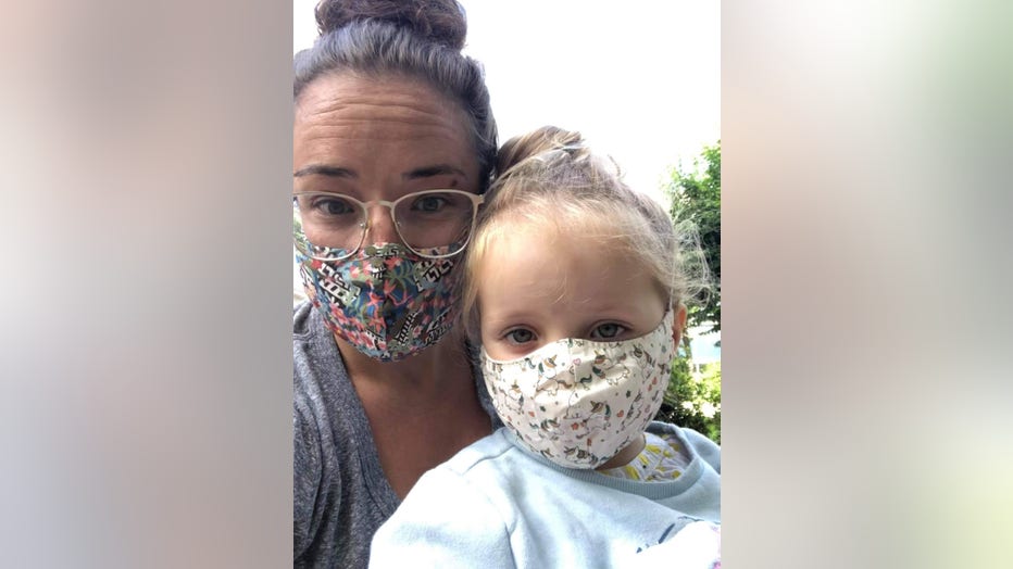 Mother and daughter, both wearing face masks, pose for a selfie.