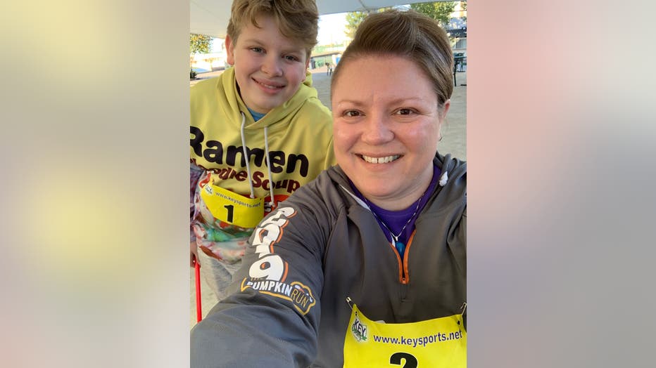 Mother and son pose at a road race, both wearing race numbers pinned to their shirts.