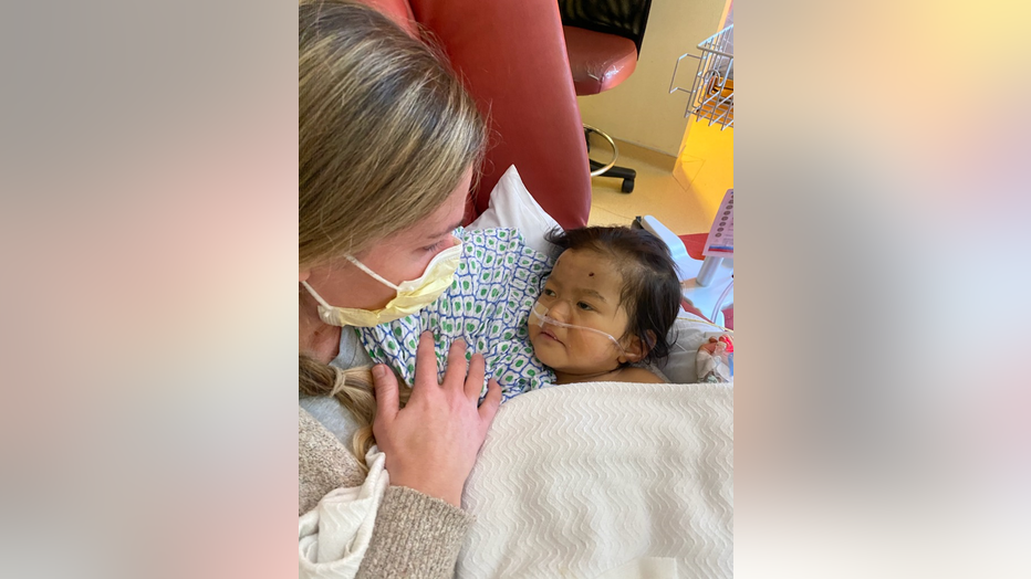 Mother wearing a mask holds her sick infant in the hospital. 