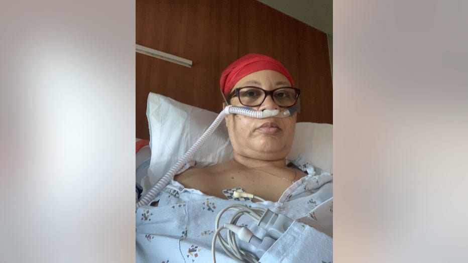 Black woman sits in hospital bed, on a machine to help her breathe.