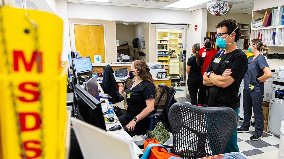 ER staff members wearing masks and scrubs look at computer monitors.