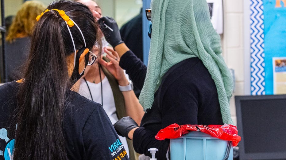 A woman in a headscarf inserts a nasal swab into another woman's nose.