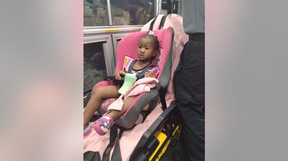 Little girl sits in car seat strapped to a gurney in the back of an ambulance.