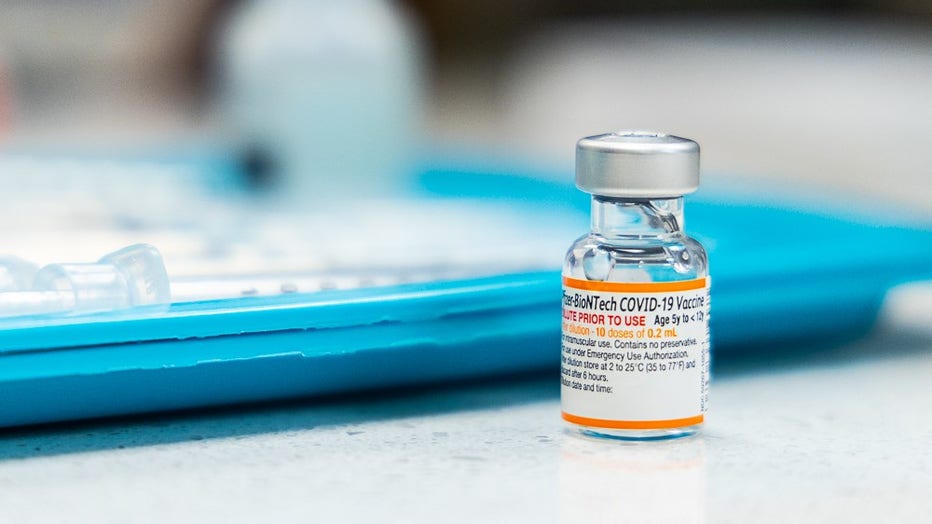 Vial of COVID-19 vaccine sits on counter next to a medical tray.