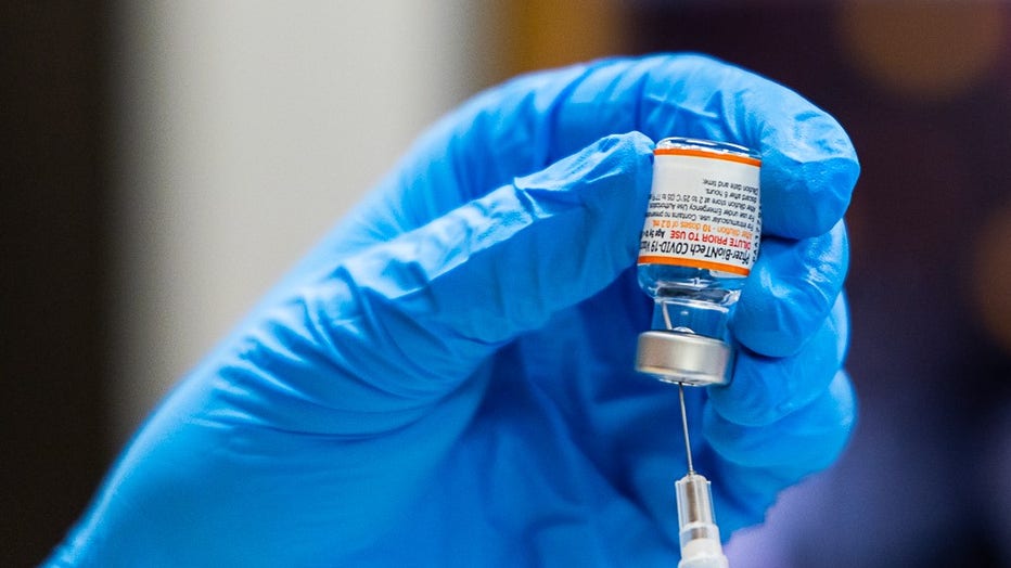 A tight shot of a gloved hand drawing the COVID-19 vaccine into a syringe.