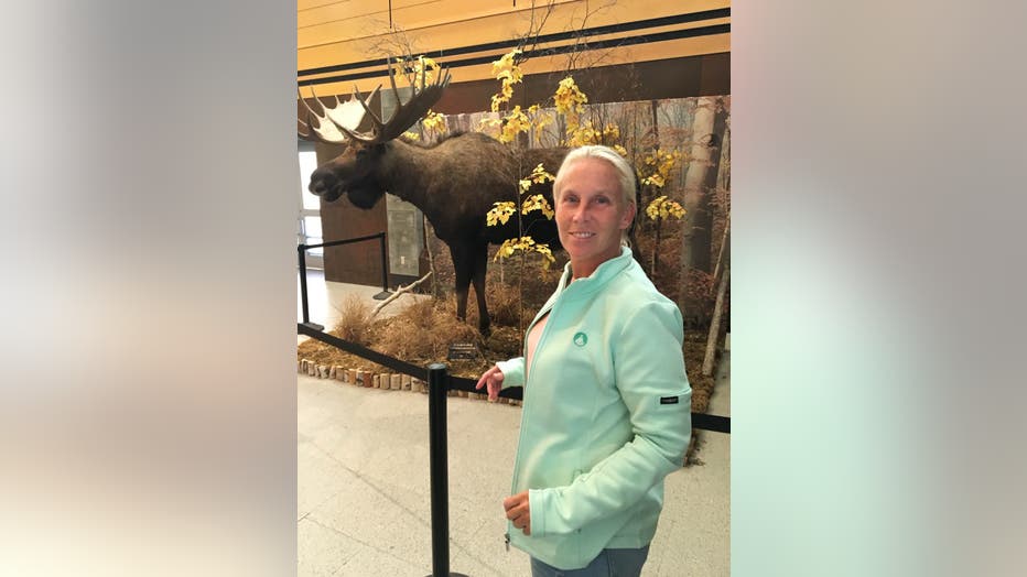 Woman with her hair pulled back smiles in front of a taxidermy elk. 