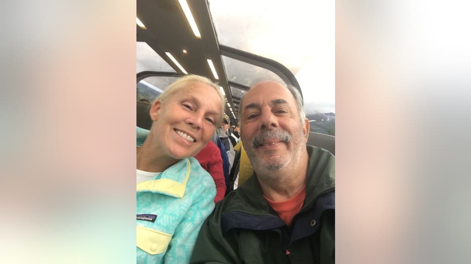 Blonde woman and her husband pose for a selfie on a train with windows above them. 