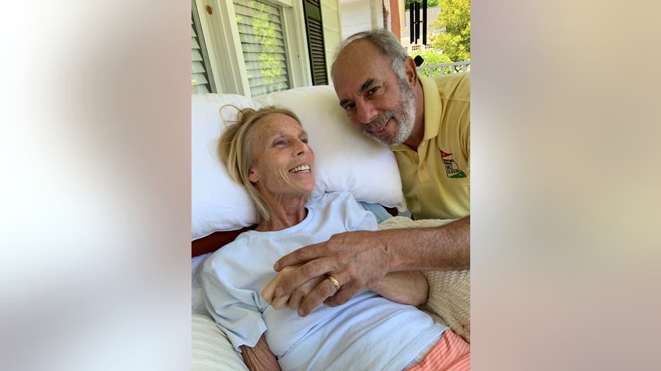 Woman with blonde hair smiles and leans back as her husband holds his hand over hers.