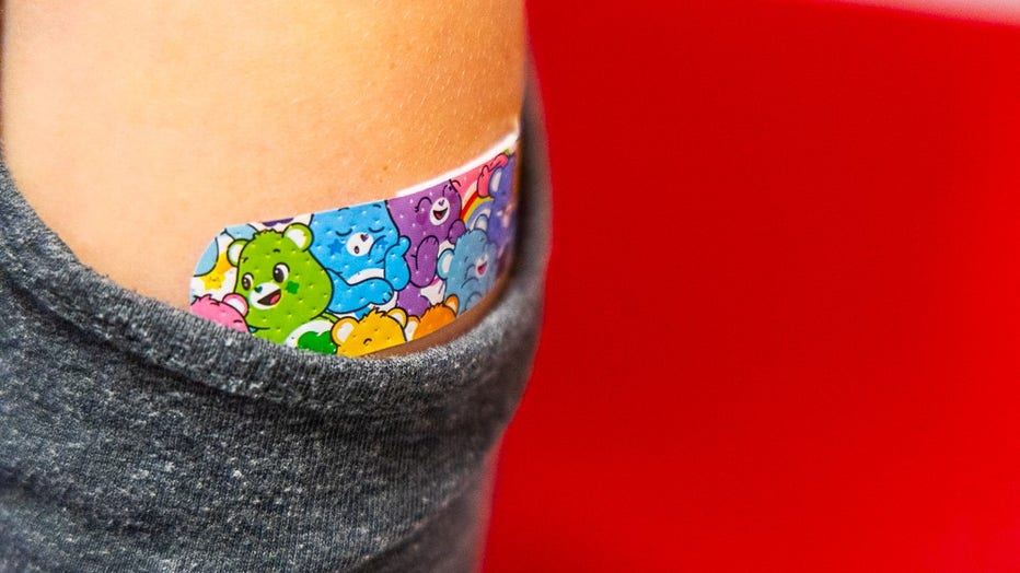 A flower BandAid covers the arm of a girl who just got a COVID-19 shot.