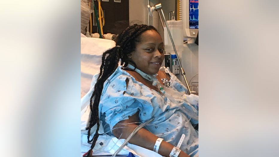 Black woman with long hair smiles from her hospital bed. She is surrounded by tubes and is pregnant.
