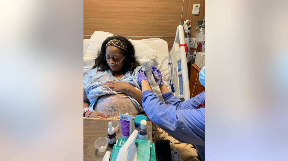 An African American woman with long hair turns her head and looks away as a nurse, just our of frame, gives her a shot. The woman is pregnant and has her hospital gown pulled up to reveal her swollen belly. 