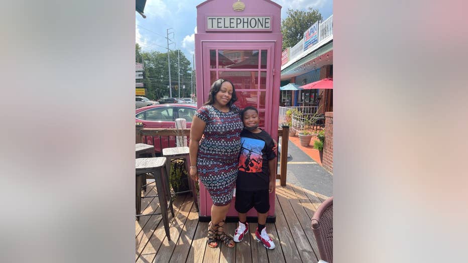 Pregnant mom hugs her 8-year-old son as they pose in front of an old English-style payphone box.