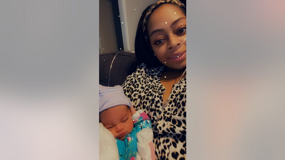 Woman wearing a leopard print top takes a selfie with her newborn daughter in her arms.