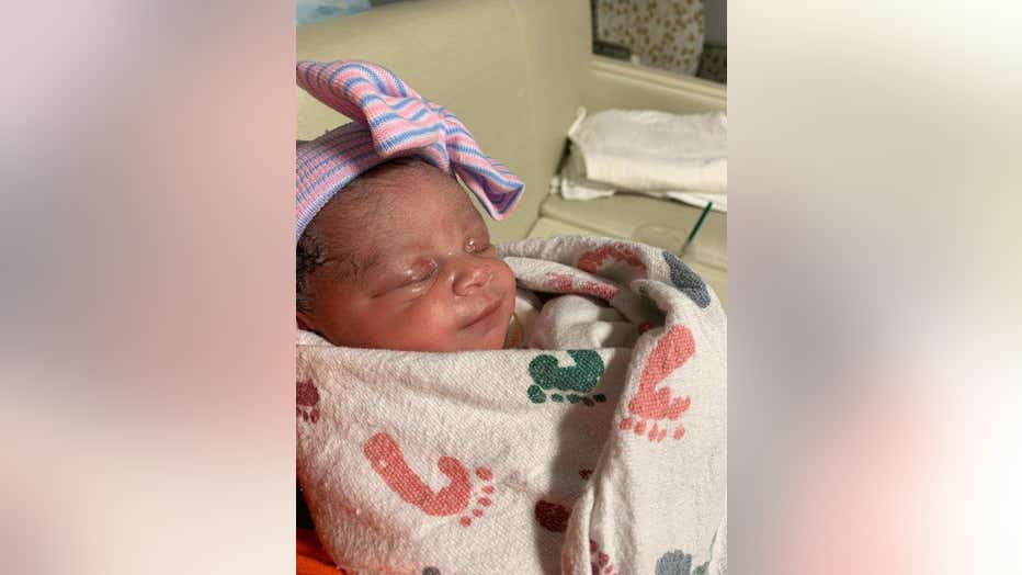 A newborn is swaddled in a pink cotton blanket and is wearing a tiny pink and blue hat.