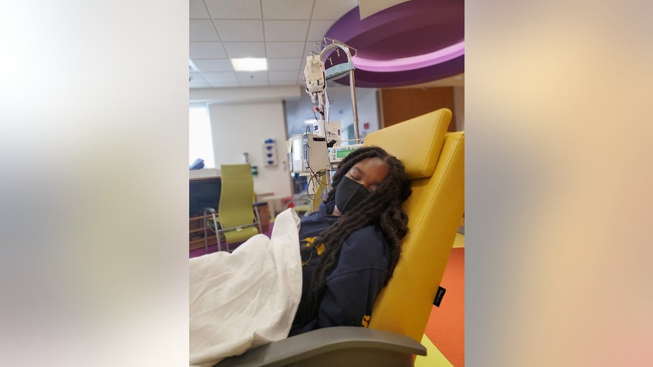 Girl wearing a facemask sits in chair undergoing a blood transfusion.
