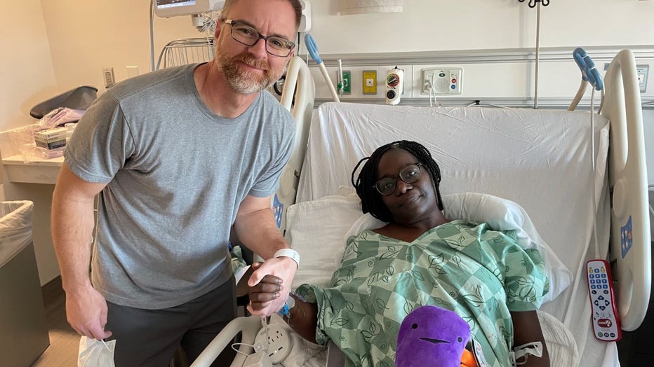 Man stands over woman in hospital bed holding her hand and smiling for a photo