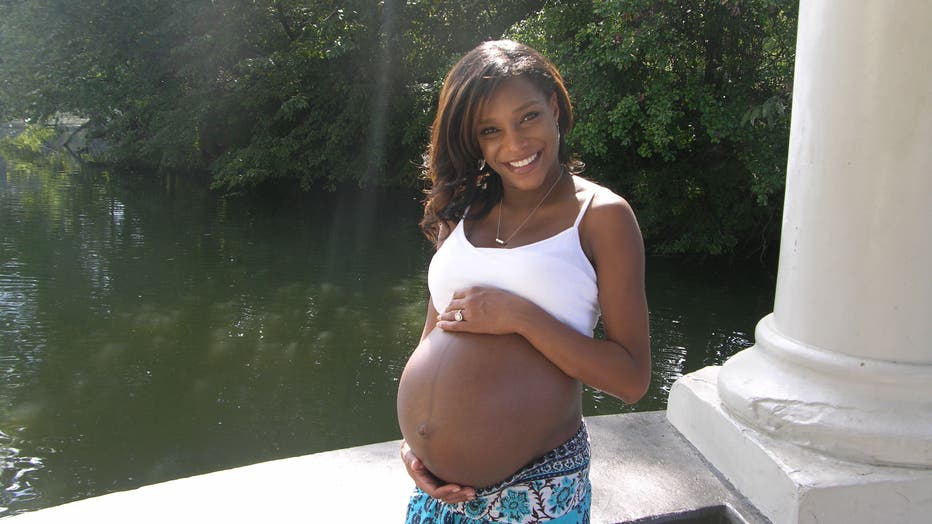 African American woman shows her pregnant belly as she smiles for the camera.