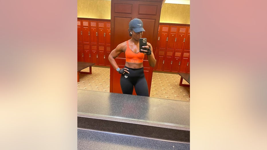 Very fit woman in workout clothes poses in front of a mirror in a gym locker room.