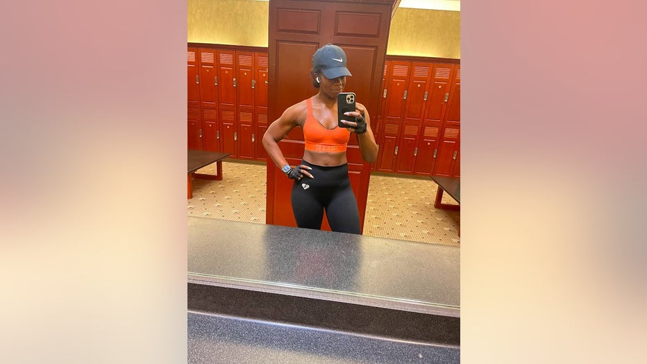 A fit woman in sportswear stands in front of a mirror in the gym locker room.