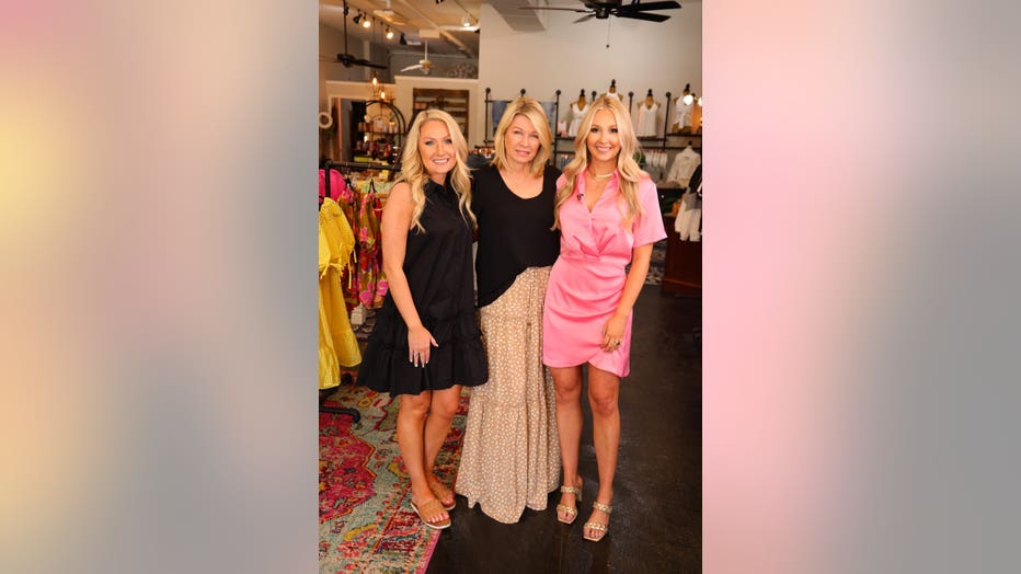 A mother stands between her two adult daughters inside their clothing store. 