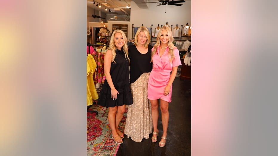 A mother stands between her two adult daughters inside their clothing store.