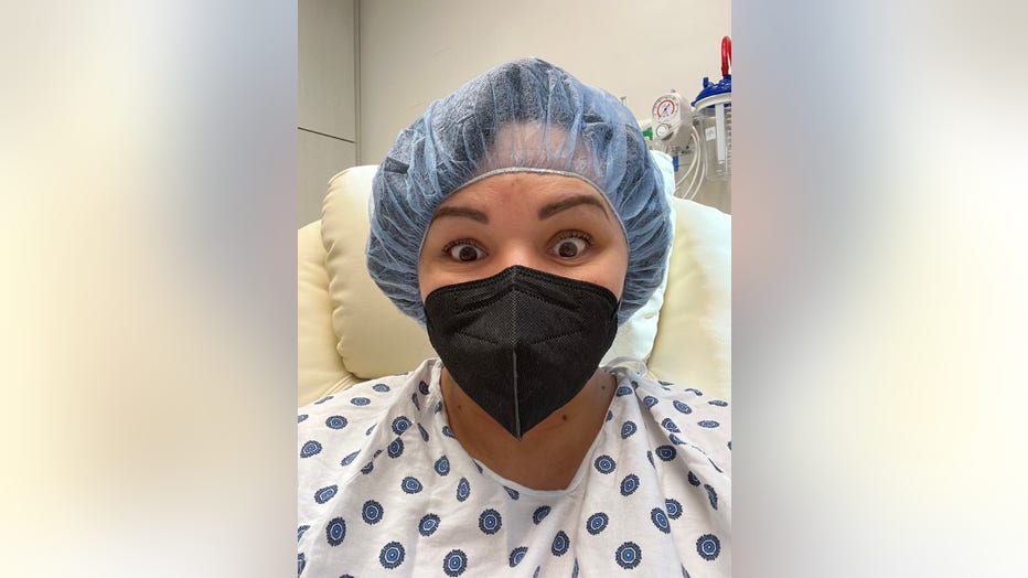 Woman in surgical cap and masks smiles for a selfie