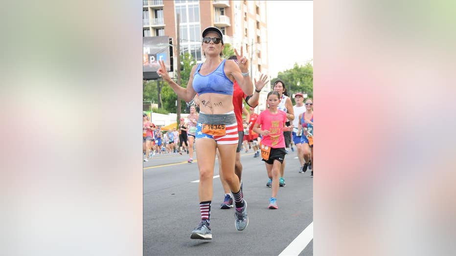 Woman lifts up her arms and smiles as she runs in a road race. 