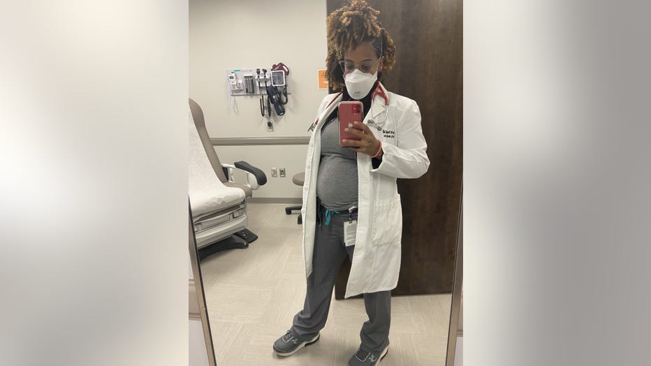 Doctor in white coat takes a photo of her reflection in the mirror, revealing her pregnant belly.