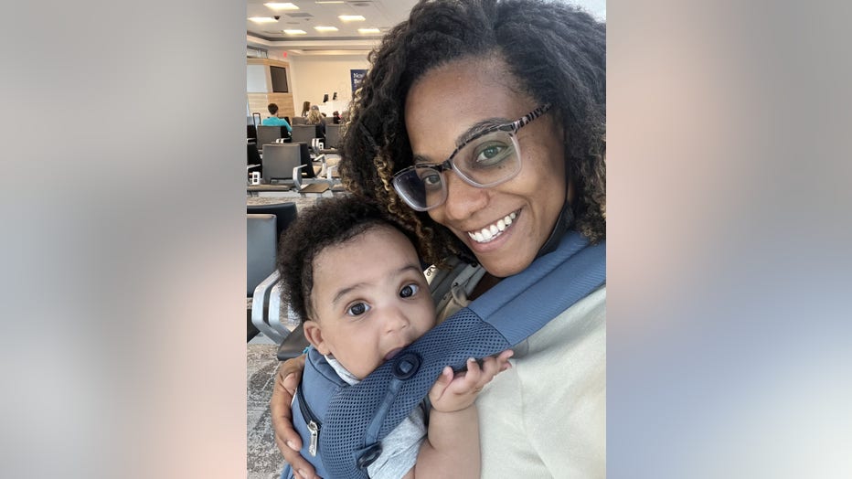 Woman poses for a selfie with her baby, who is strapped to her chest.