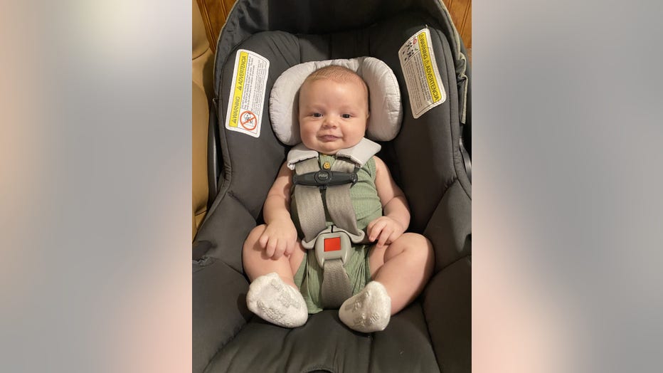 Baby boy strapped into car seat smiles. 
