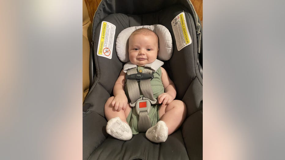 Baby boy strapped into car seat smiles.