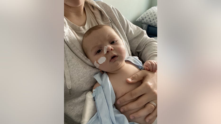 A young baby with a feeding tube in nose leans back against his mothers chest in the hospital.