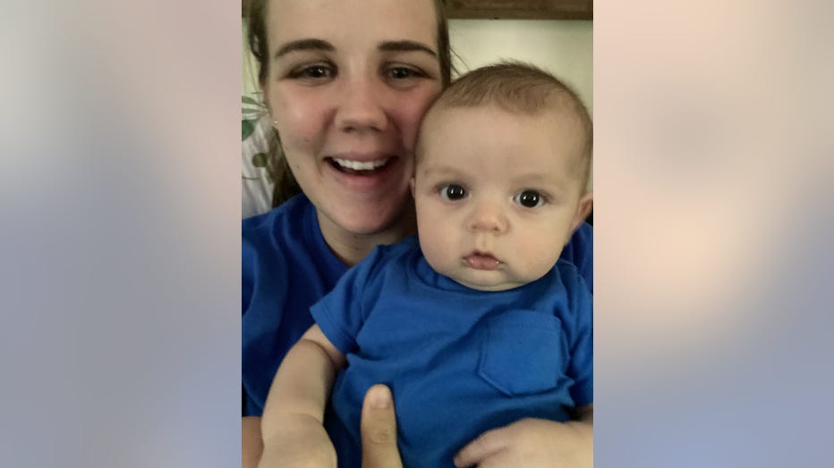 A young mom smiles while taking a selfie with her 3-month-old son in her lap. 