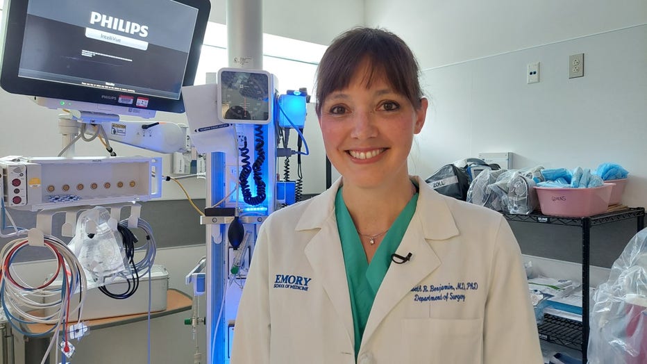 Doctor in white coat stands in a trauma bay surrounded by medical equipment.